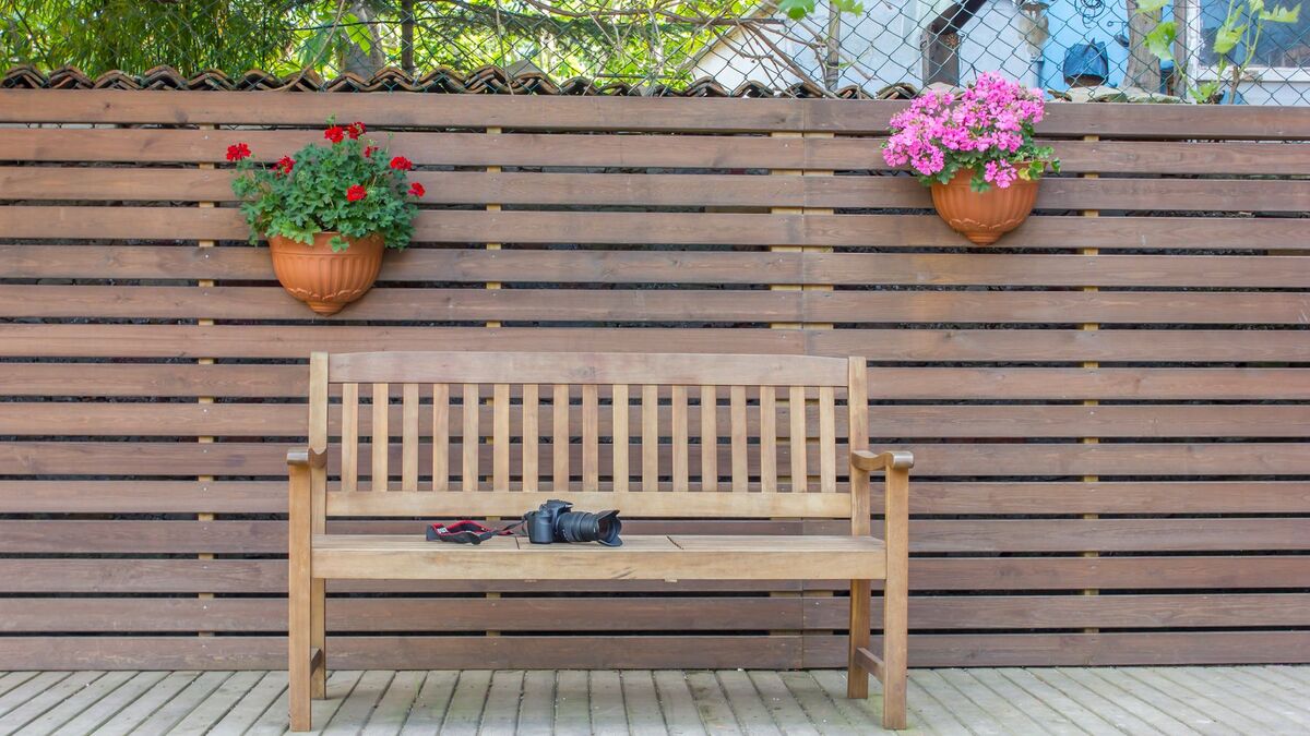 A horizontal slatted privacy fence behind a wooden bench, with two hanging flower pots on the boards