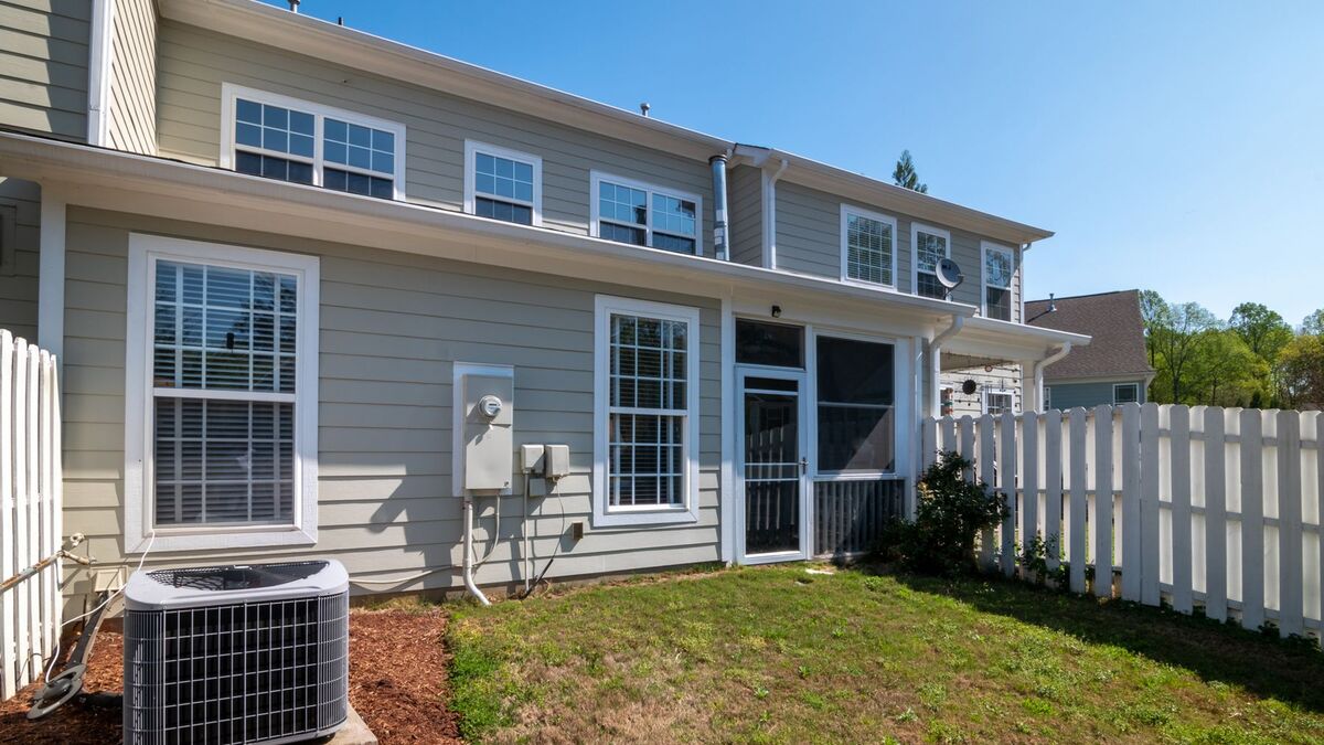 The back of a two-story house with a small lawn and a white vinyl privacy fence running along the property line